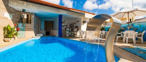 A swimming pool with a water feature, outdoor seating, and a mural on the wall.