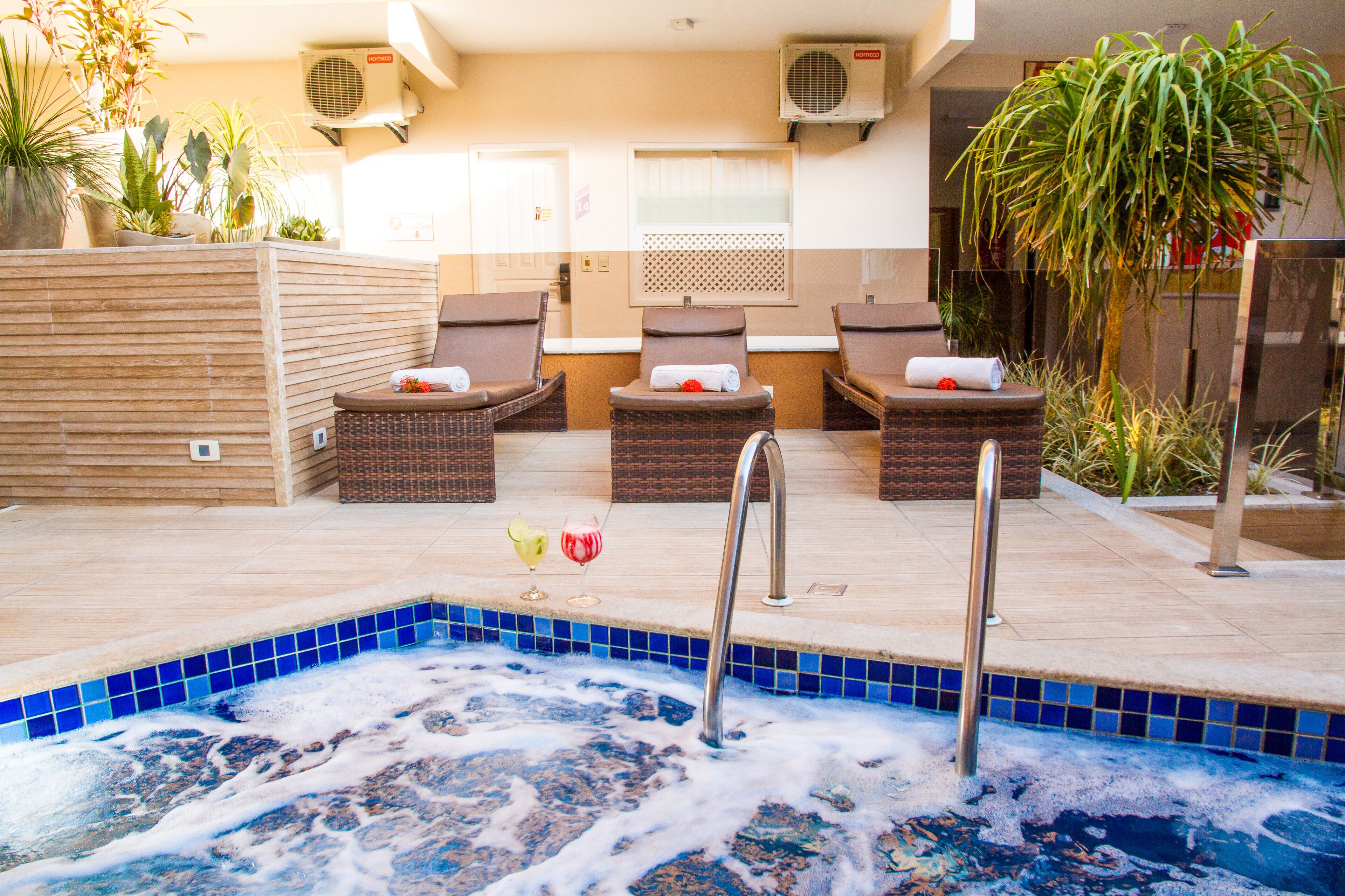 Een wellnessruimte met een jacuzzi, lounge fauteuils en potplanten.
