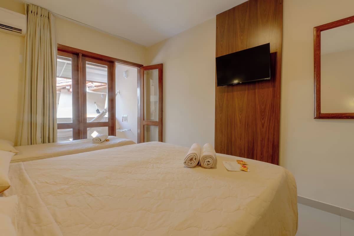 A hotel room with two beds, a TV mounted on the wall, and a window with curtains.