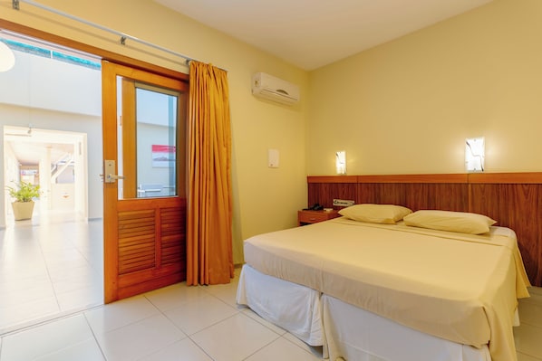 Une chambre d’hôtel équipée d’un lit, de rideaux, d’un climatiseur, d’une table de chevet et d’une lampe fixée au mur.