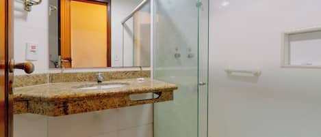 Un baño con lavamanos de encimera de granito, cabina de ducha con mampara de vidrio y espejo sobre el lavamanos.