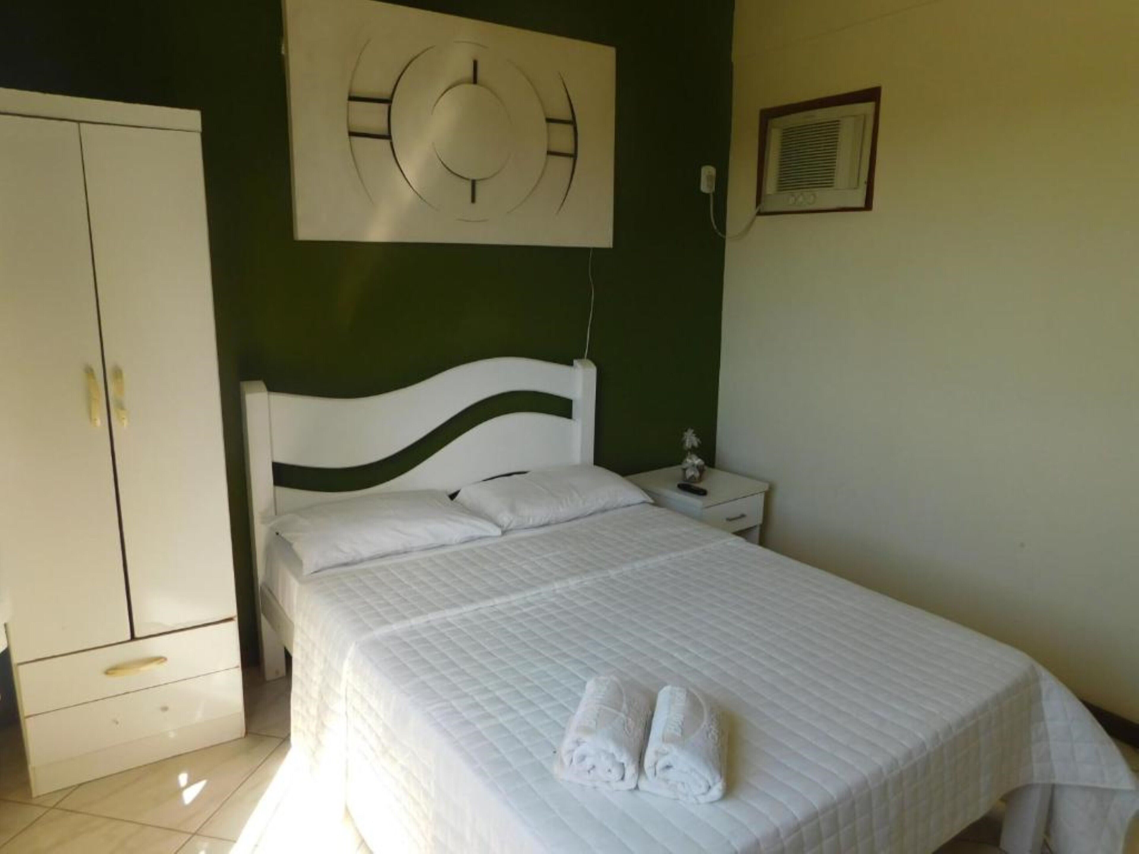 A bedroom with a bed, white headboard, and a wall-mounted clock.