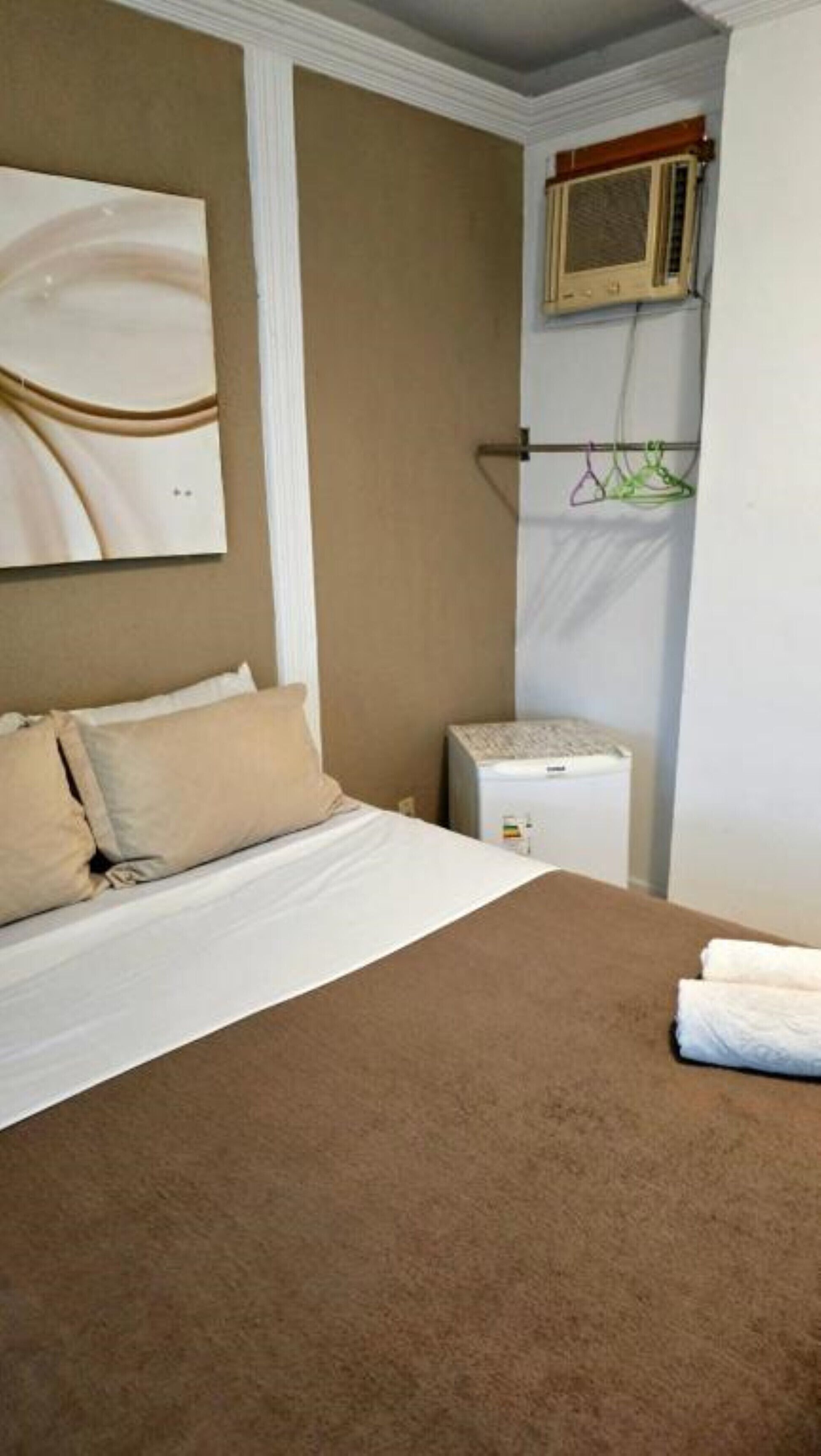 A hotel room with a bed, a small heater, and a wall-mounted air conditioning unit.