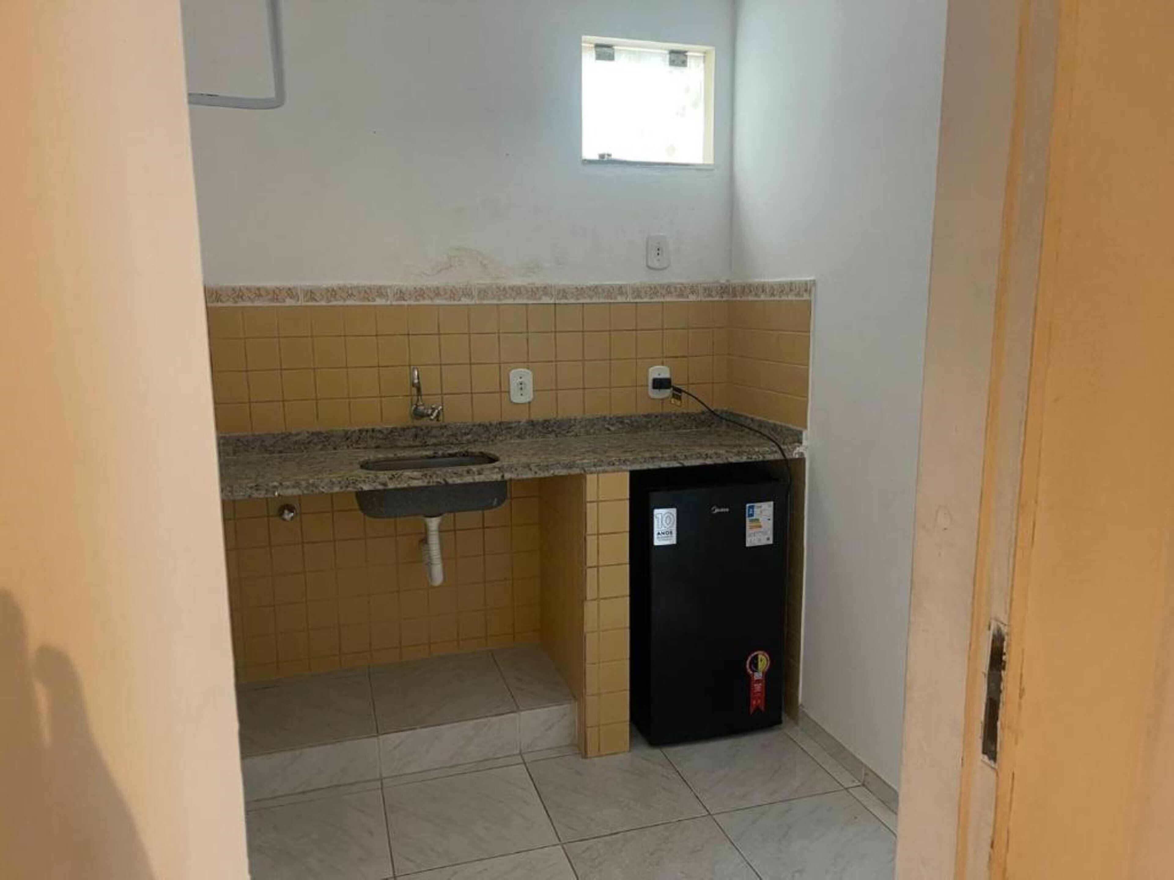 Una cocina pequeña con un lavamanos, una ventana y un refrigerador.