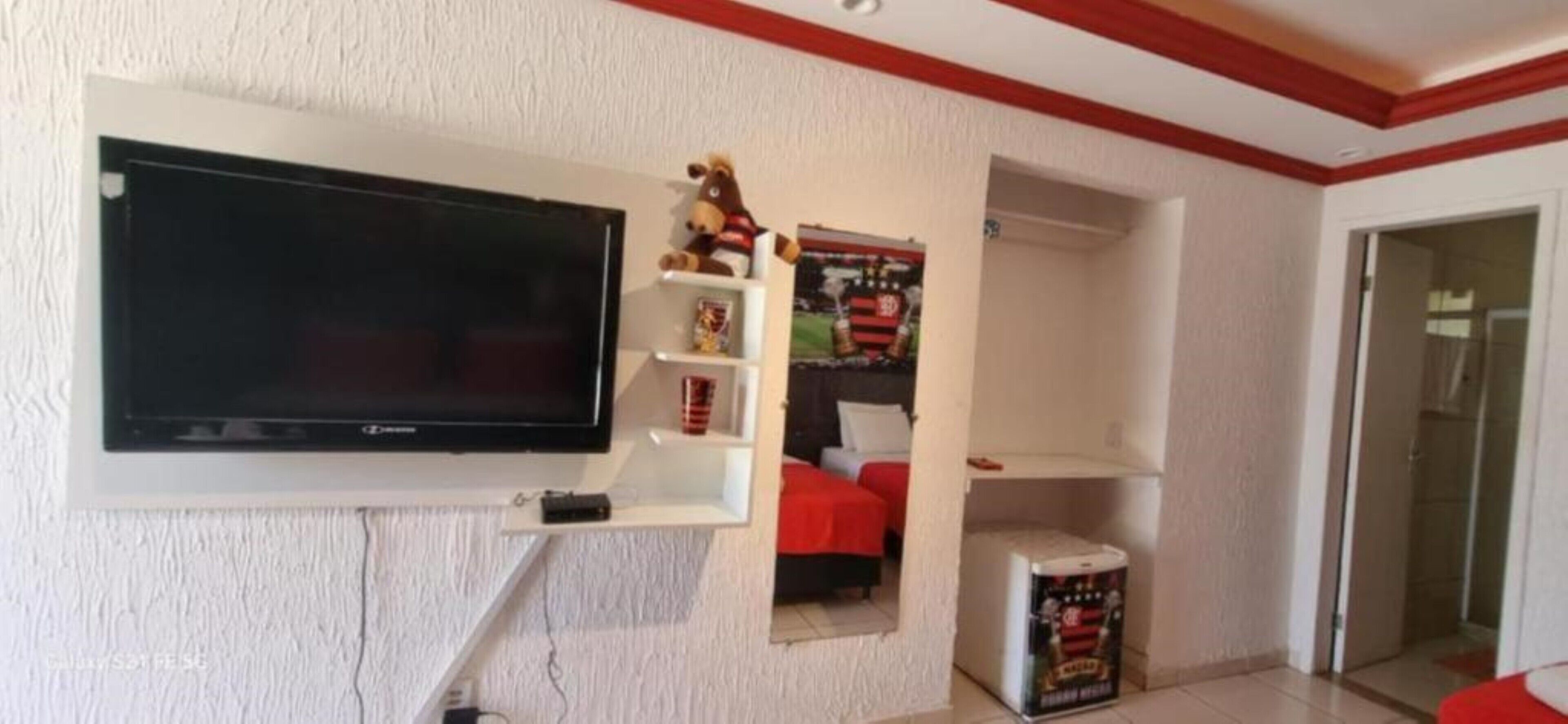 A living room with a mounted TV, a shelf with a stuffed toy, and a poster on the wall.