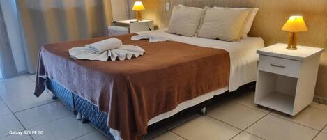 A hotel room with a bed, two bedside tables with lamps, a nightstand, and a tiled floor.