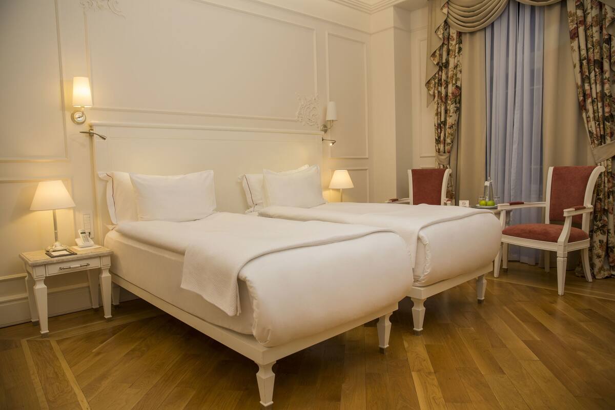 A hotel room with two beds, a chair, a nightstand, and a lamp.
