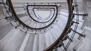 Un escalier en colimaçon avec une rampe métallique et un sol réfléchissant.