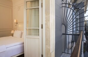 Ein Hotelzimmer mit Bett, einem Fenster mit Vorhängen, einer Wandlampe und einem Metall-Geländer für eine Treppe.