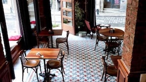 Un café chaleureux avec des tables et des chaises en bois, un sol à motifs et de grandes fenêtres donnant sur la rue.