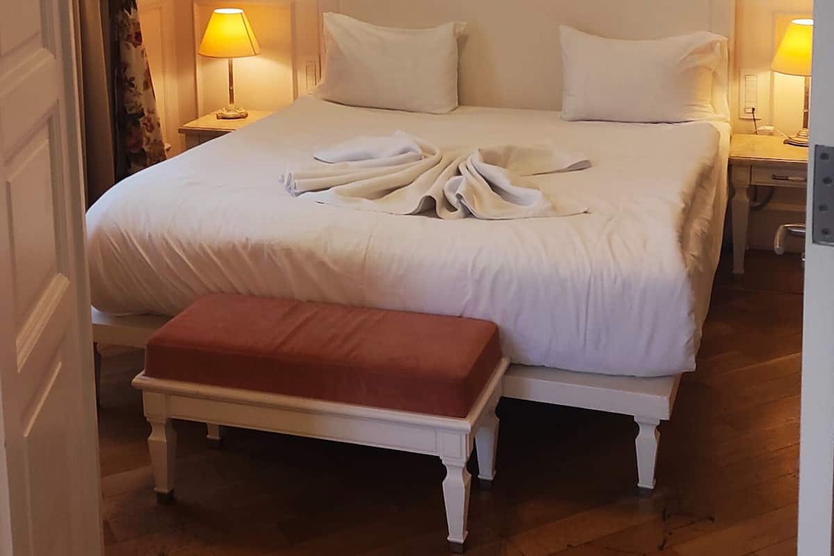 A hotel room with a large bed, two bedside lamps, a wooden floor, and a door with a floral curtain.