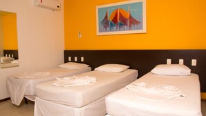 A hotel room with three single beds, a large mirror, an air conditioning unit, and a painting on the wall. - Saint Patrick Praia Hotel (Maceió)