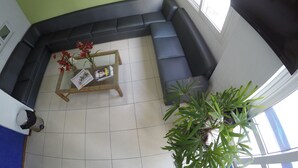 A living room with a green wall, a black sofa, a coffee table with magazines and flowers, and a large window. - Saint Patrick Praia Hotel (Maceió)