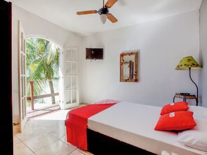 A bedroom with a bed, a ceiling fan, a window with a view of palm trees, and a door leading outside. - Pousada Recanto Shangri-la (Cabo Frio)