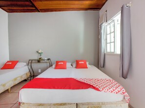 A hotel room with two beds, each with a red pillow, a small table with a vase, and a window with curtains. - Pousada Recanto Shangri-la (Cabo Frio)