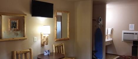 Habitació d'hotel amb una cadira de fusta, una taula petita, televisió penjada, un mirall, una taula de planxar i un aparell d'aire condicionat.