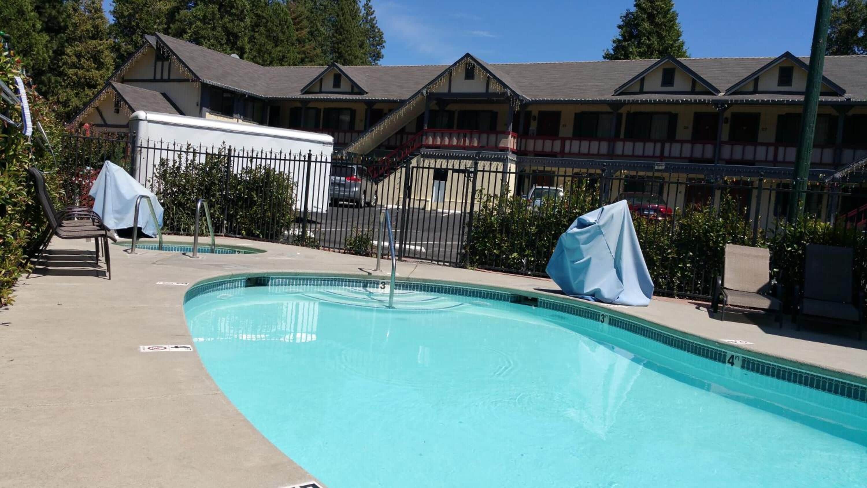 A swimming pool with a covered bench, a fence, and a building with a sloped roof in the background.