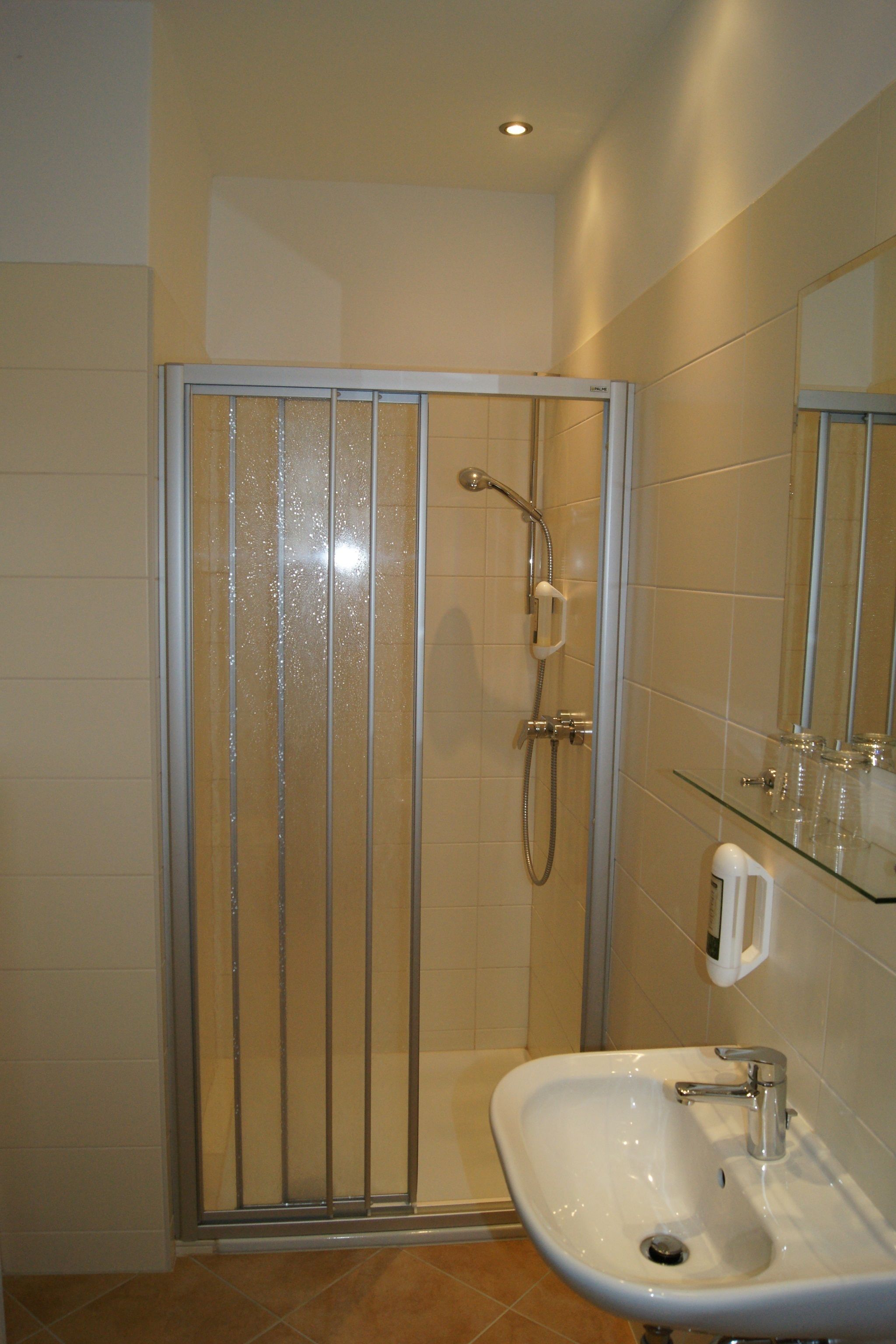 Une salle de bain avec une douche à parois de verre, un lavabo avec un miroir et une étagère en verre où sont rangés les articles de toilette.