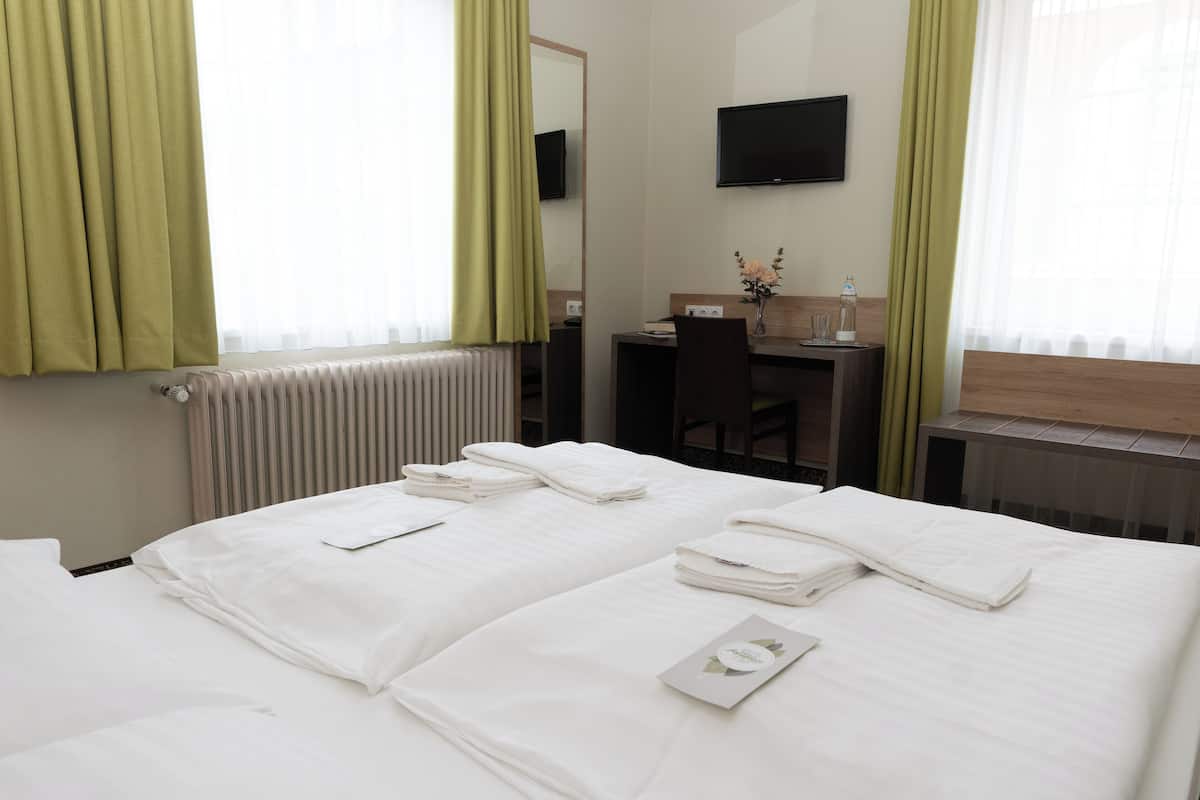 A hotel room with two beds, a desk, a chair, a TV, and a radiator.