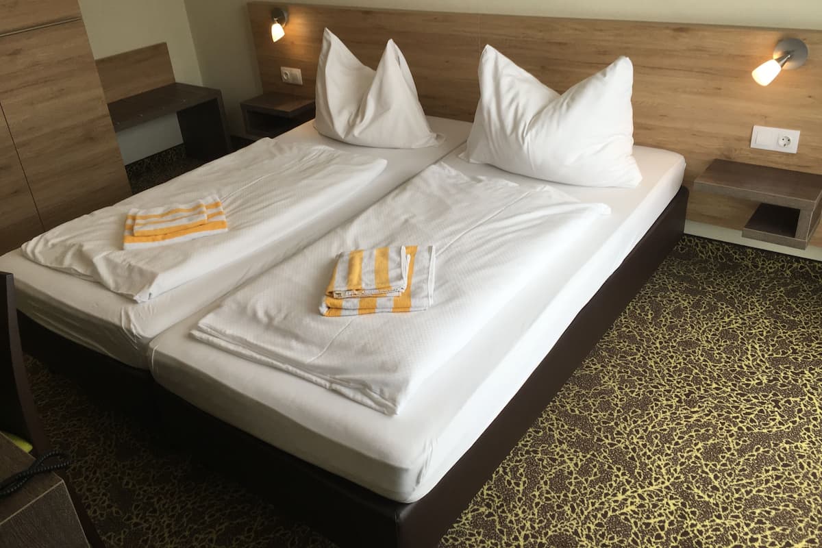 A double bed with white linens and two pillows, a wooden headboard, bedside tables with lamps, and a leopard print carpet.