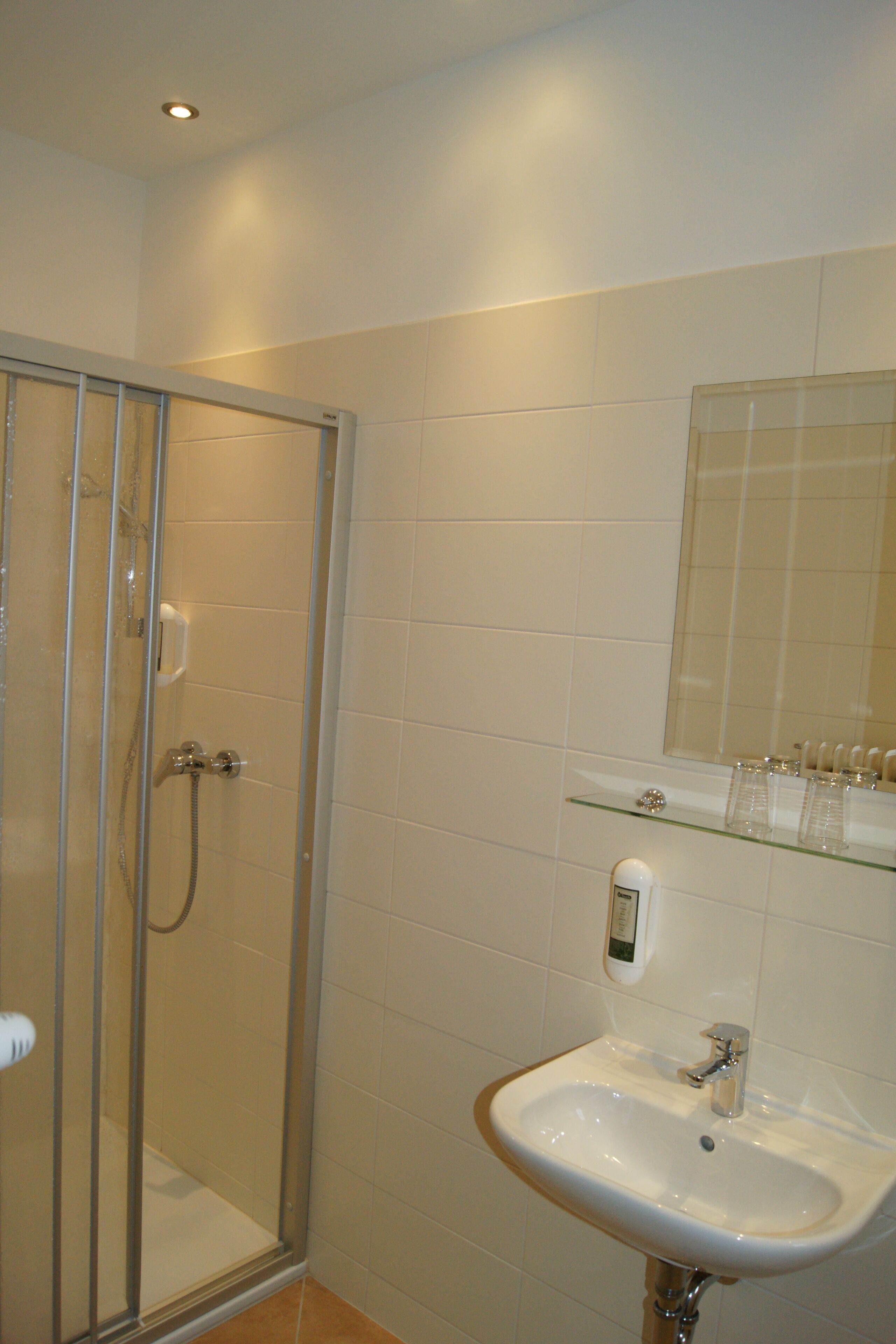 Een badkamer met een glazen douchecabine, een wit wastafelmeubel en een spiegel erboven.