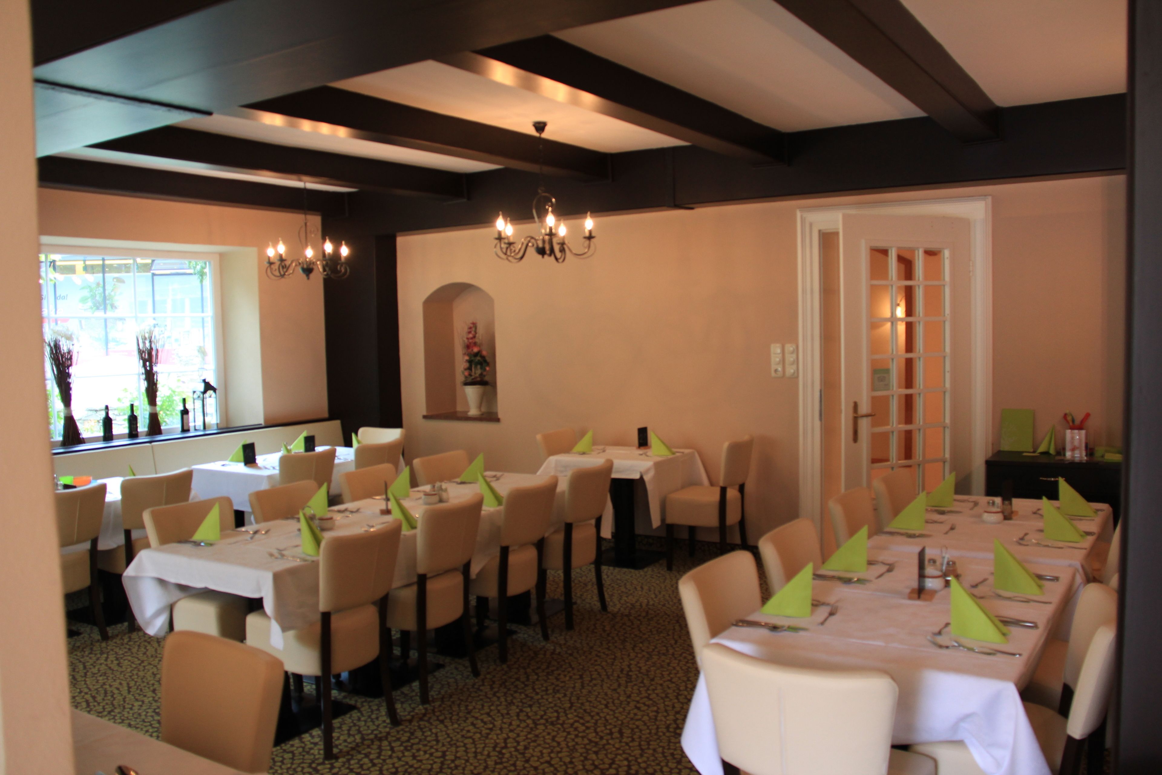 Une salle à manger avec plusieurs tables dressées, des chaises et un lustre.