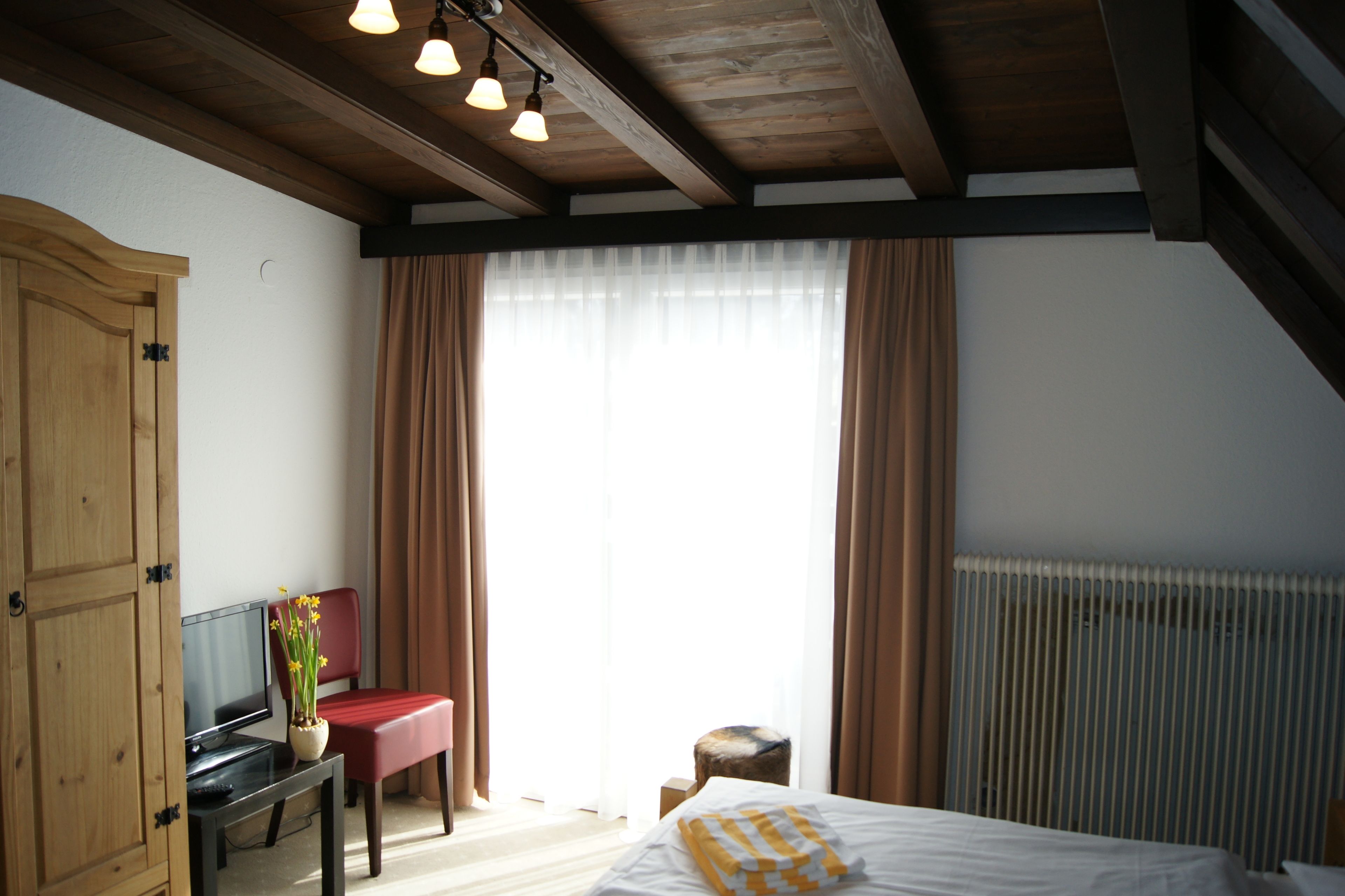 A bedroom with a bed, a desk with a computer, a chair, a window with curtains, and a radiator.