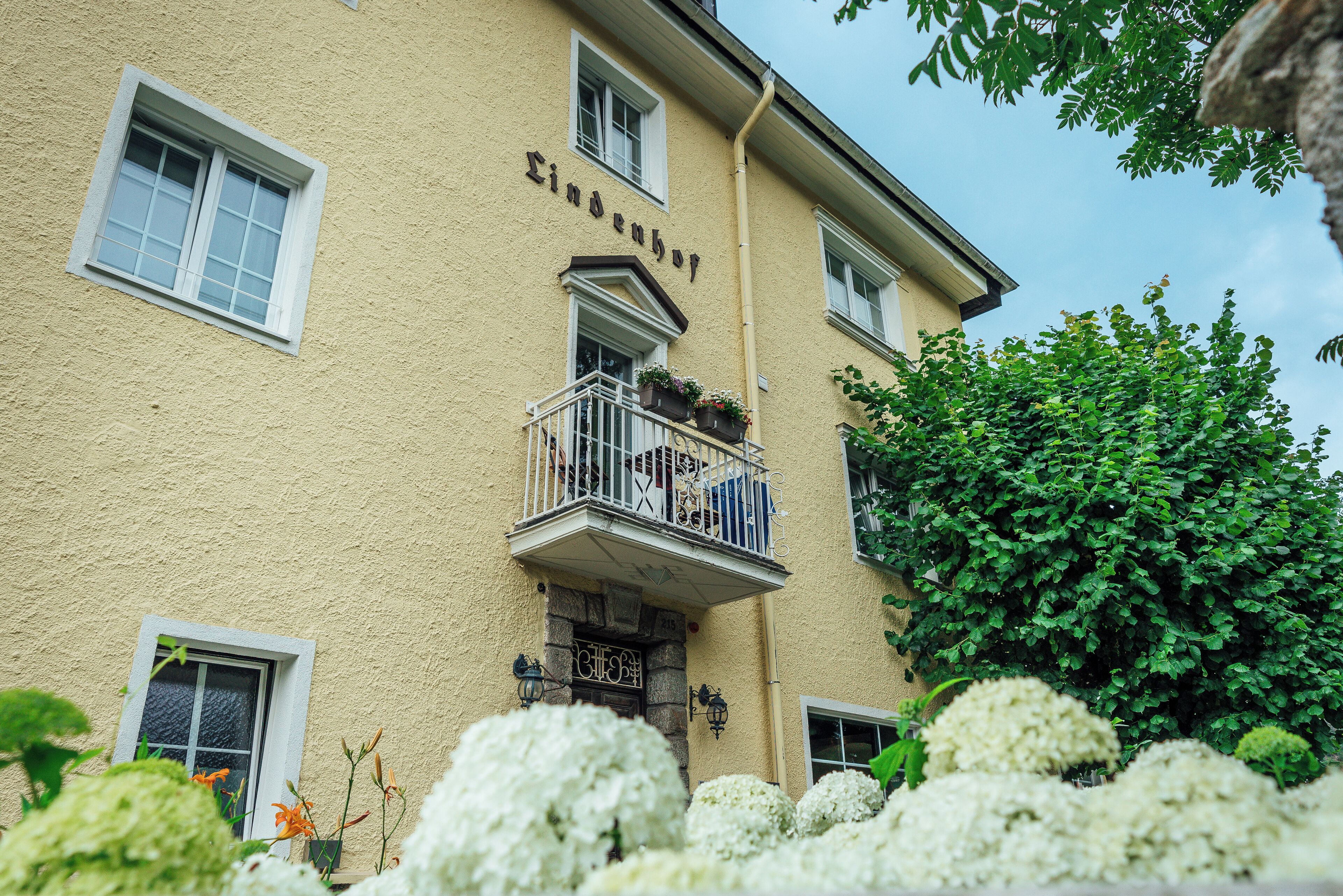 A building with a balcony, a sign reading "Lindenhof," and lush greenery around it.