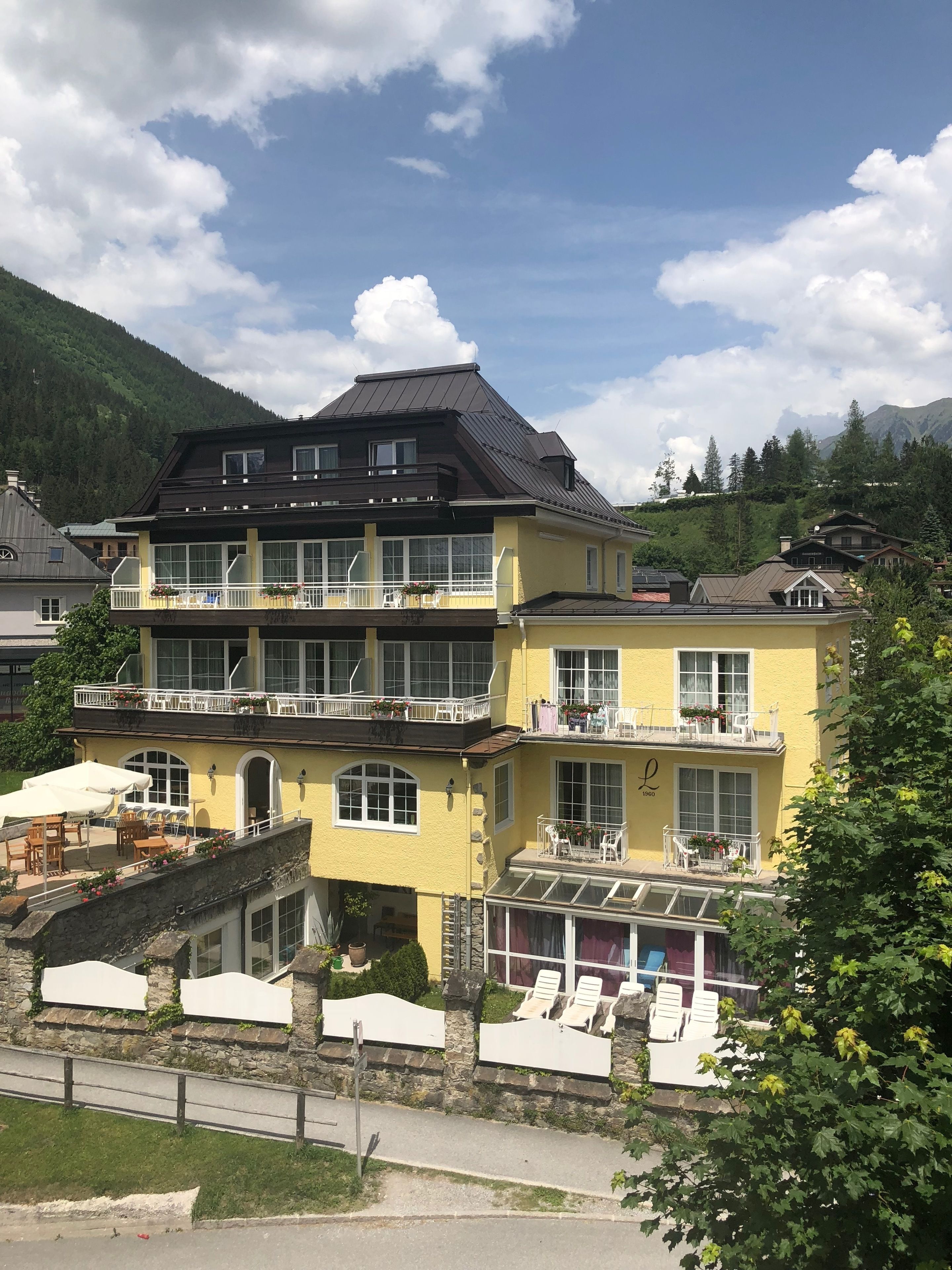 A two-story building with balconies, outdoor seating, and a mountain backdrop.