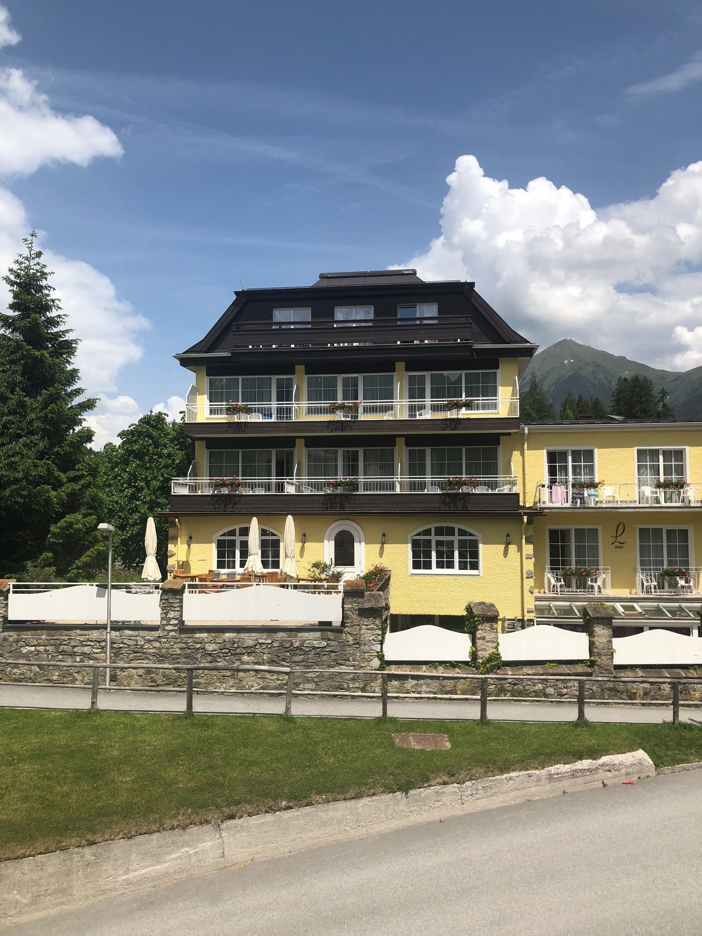 Un edificio de varios pisos con balcones, un muro de piedra al frente y una montaña al fondo.