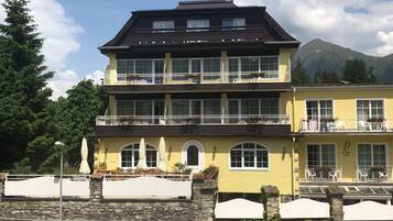 Un edificio de varios pisos con balcones, un muro de piedra al frente y una montaña al fondo.