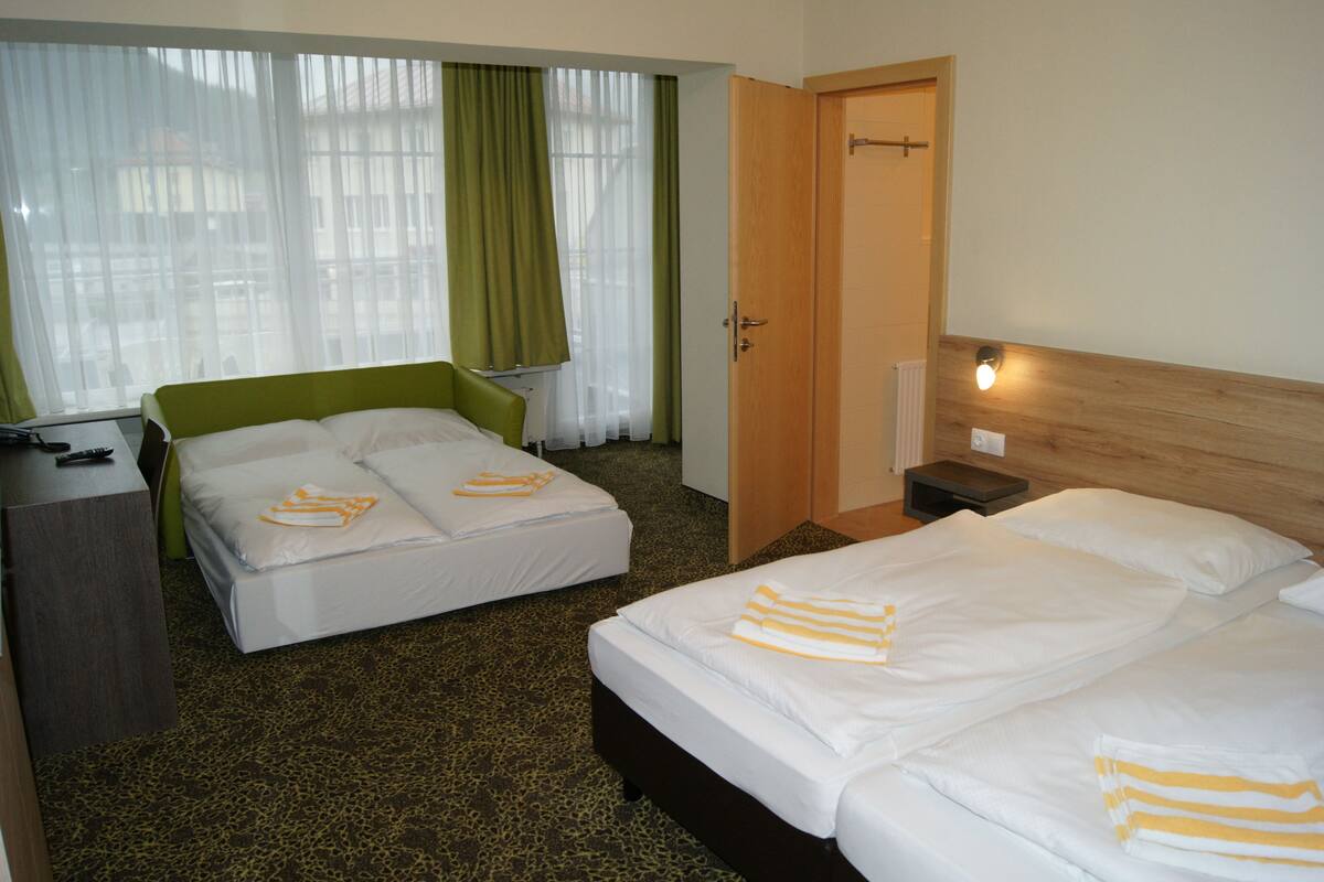 A hotel room with two beds, a desk, a chair, and a window with curtains.
