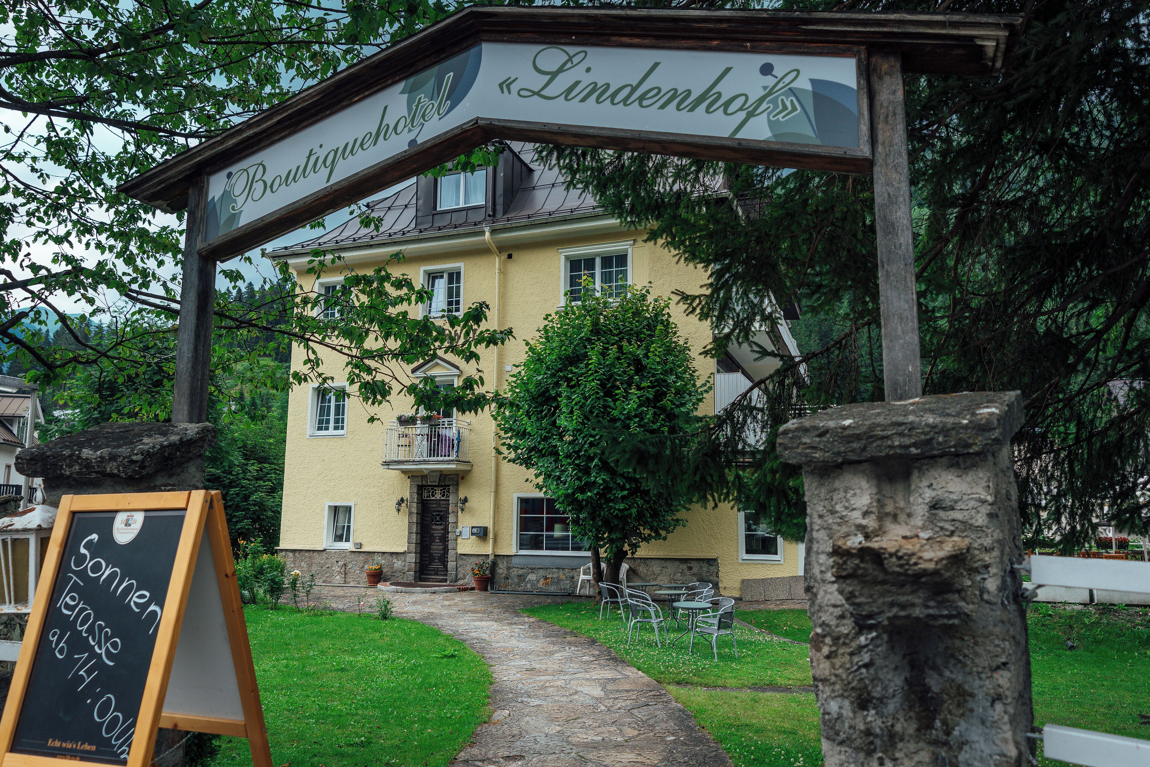 A boutique hotel entrance with a sign reading "Boutiquehotel Lindenhof" and a chalkboard sign advertising "Sonnen Terasse ab 14.00 Uhr."