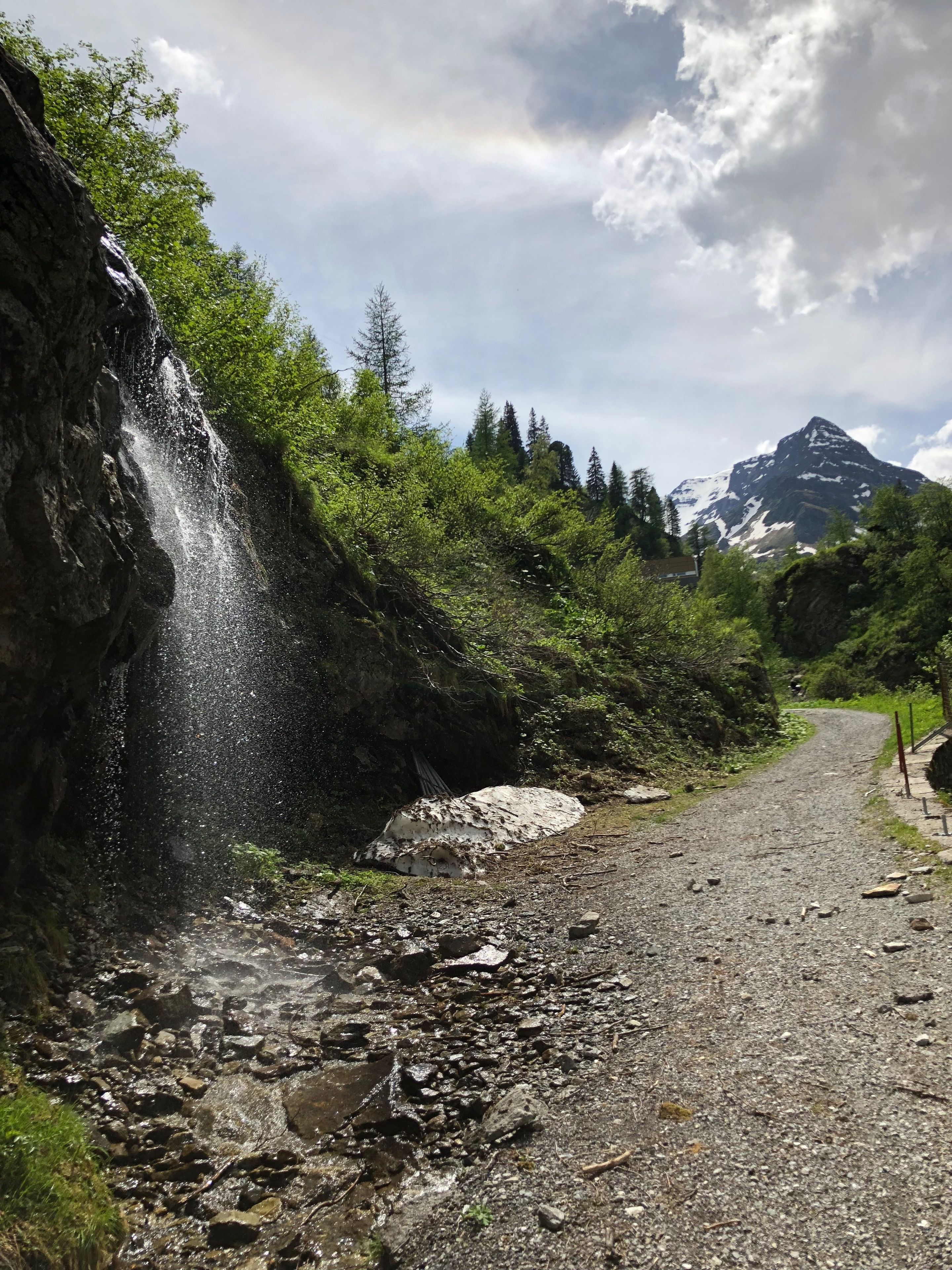 A gravel path leading to a waterfall with a mountain in the background.