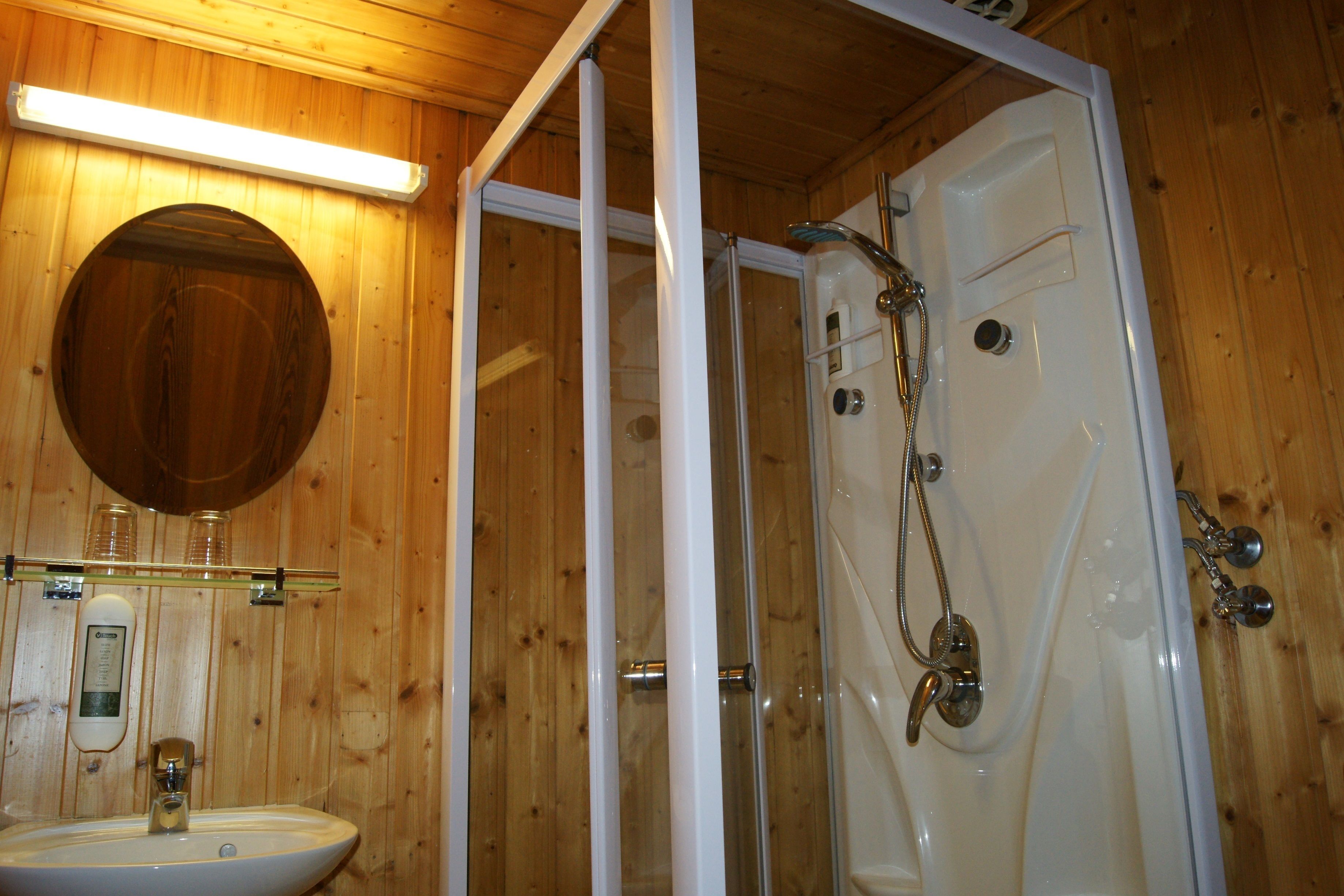 A wooden interior with a glass-enclosed shower, a sink, and a mirror.