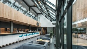 A modern interior with a reception desk, seating area, and a high ceiling with skylights. - Regatta Hotel Restauracja Spa (Poznan)
