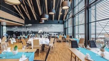 A modern dining area with wooden tables, chairs, and pendant lighting.