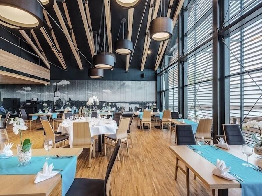 Uma zona de refeições moderna com mesas e cadeiras de madeira, e iluminação pendente.