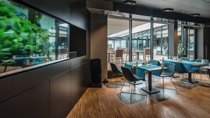 A modern dining area with tables and chairs, large windows, and a view of greenery outside. - Regatta Hotel Restauracja Spa (Poznan)