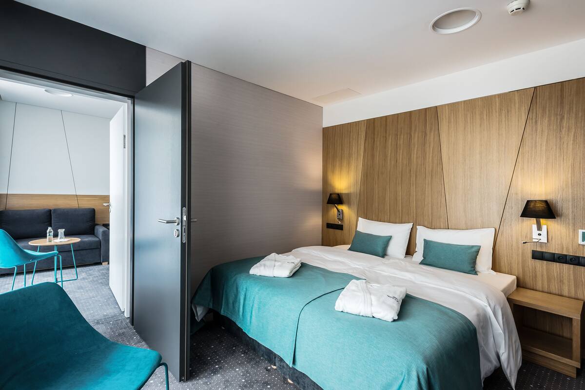 A modern hotel room with a bed, a seating area with a sofa and chairs, and a wooden accent wall.