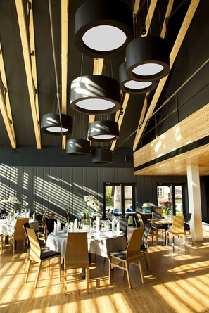 A modern restaurant with multiple tables set for dining, featuring a high ceiling with exposed beams and pendant lighting. - Regatta Hotel Restauracja Spa (Poznan)