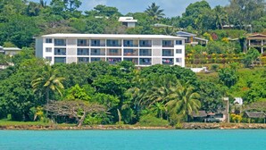 Un hotel de varios pisos con balcones, rodeado de exuberante vegetación y vistas al mar.