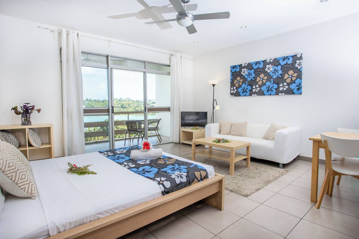 A modern hotel room with a bed, a sofa, a TV, and a balcony with a view.