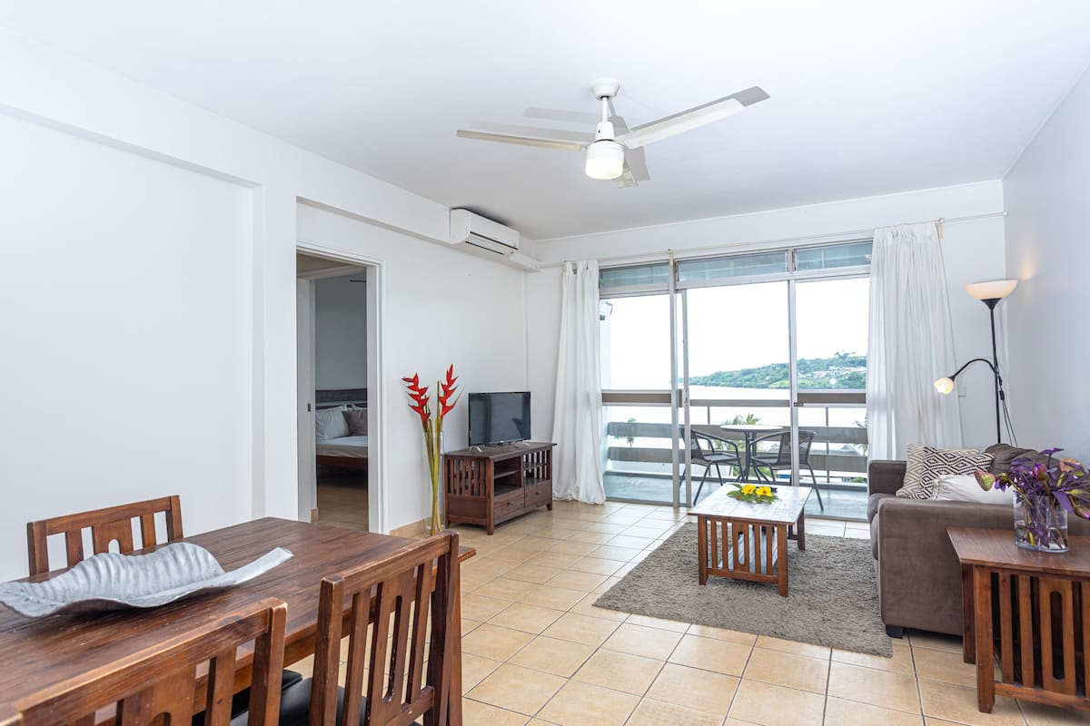 A spacious living room with a wooden dining table, a sofa, and a TV.