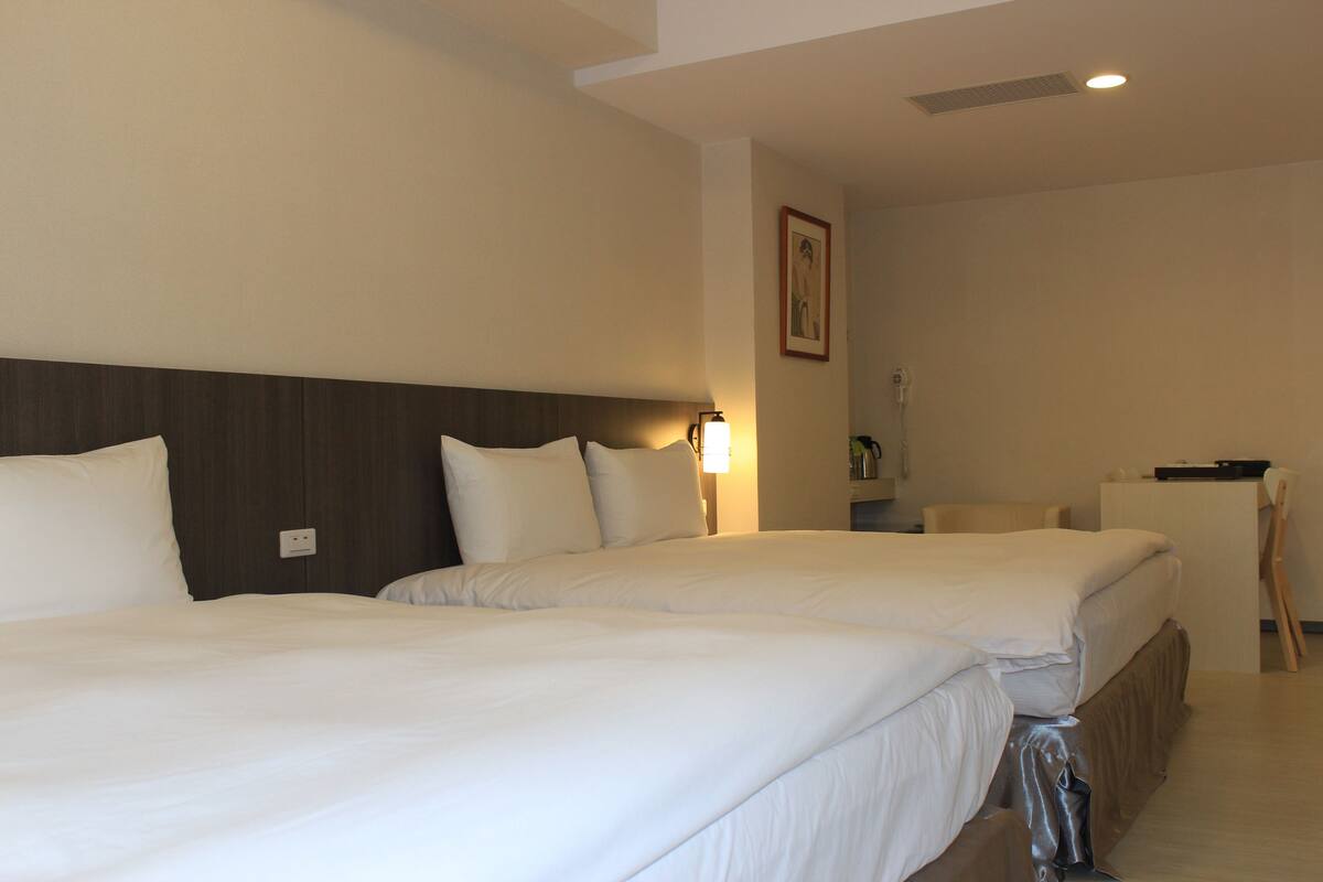 A hotel room with two beds, a desk, and a chair.