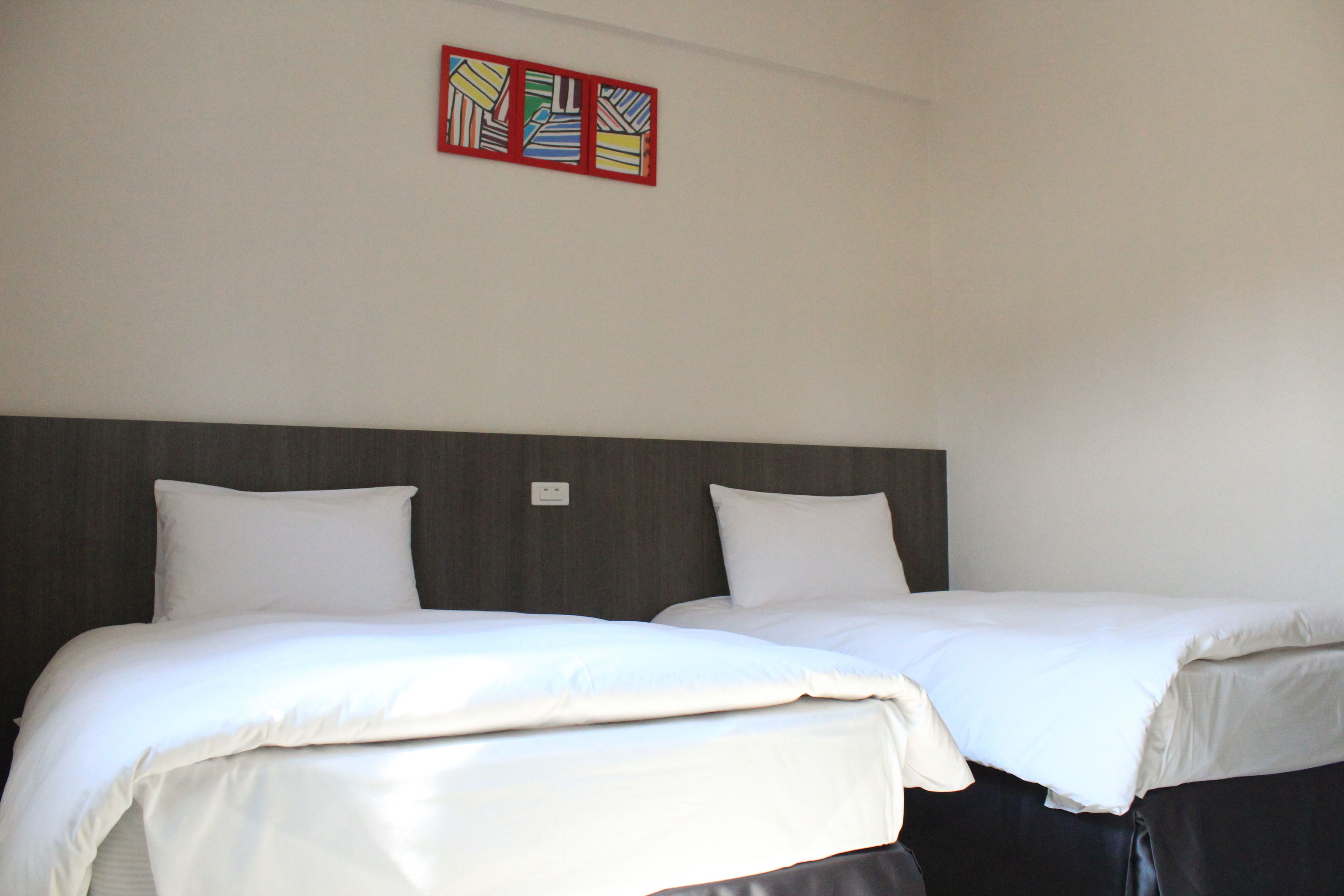 A hotel room with two beds, a wooden headboard, and a colorful artwork above the beds.