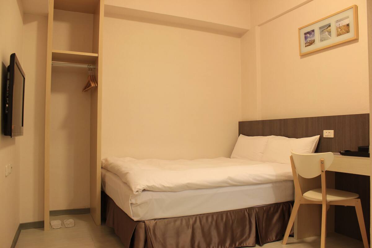 A neatly made bed with a brown skirt, a wooden chair, and a desk with a computer.