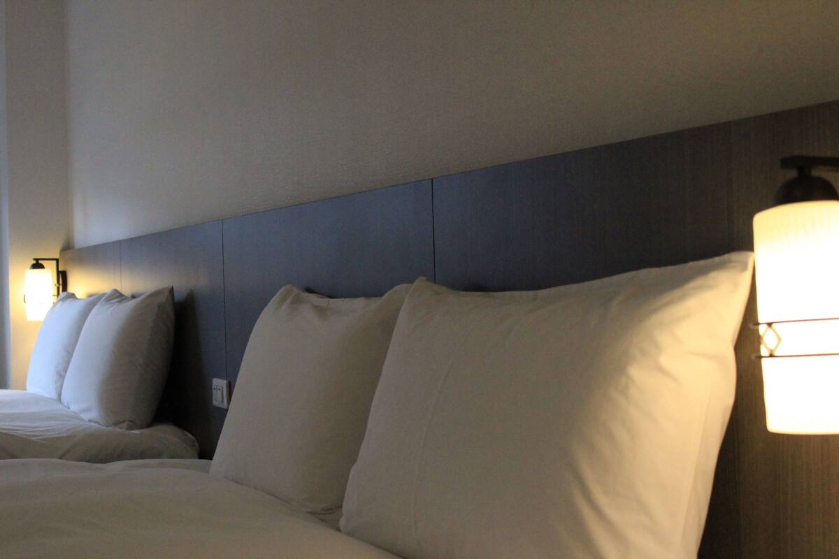 A hotel room with a large bed, multiple pillows, and a wall-mounted light fixture.