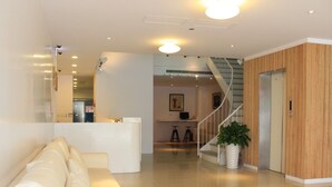Un área de recepción moderna con un mostrador blanco, una escalera y una planta en maceta.