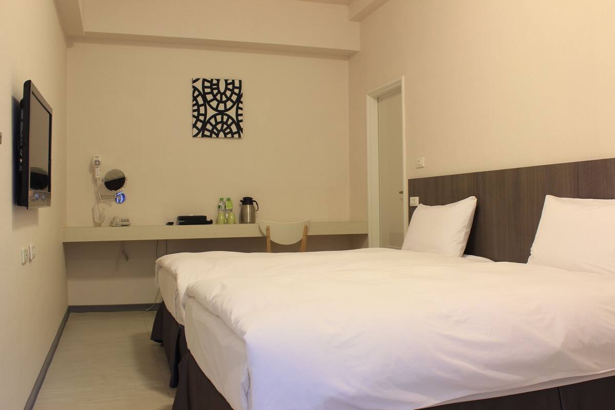 A hotel room with a bed, a desk with a chair, a mirror, and a wall decoration.